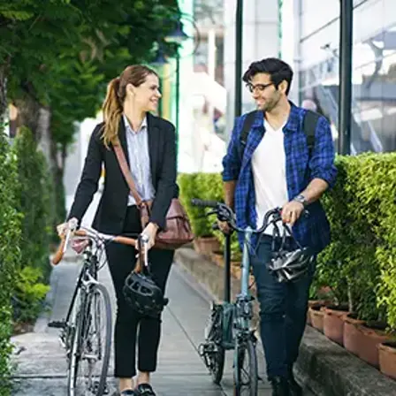 Two colleagues walking with bicycles along a pavement while talking.