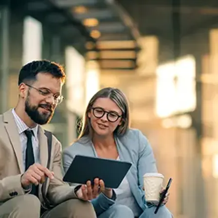 Two colleagues reviewing a tablet while seated outside an office.