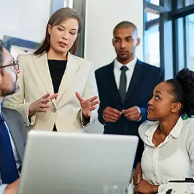 Four colleagues discussing work around a laptop in an office.