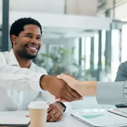 A smiling businessman shaking hands across a desk during an office meeting.
