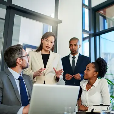 Four colleagues discussing work around a laptop in an office.