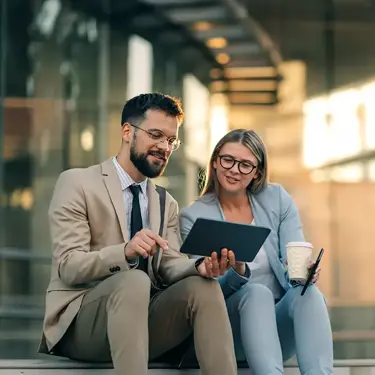Two colleagues reviewing a tablet while seated outside an office.
