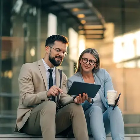 Two colleagues reviewing a tablet while seated outside an office.